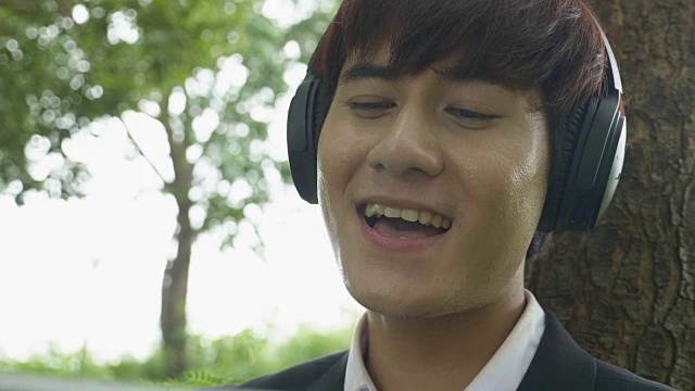 亚洲年轻男性在秋季公园用无线耳机听音乐-播客视频下载