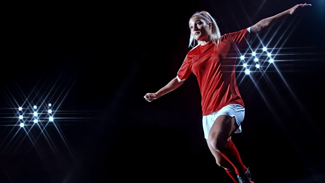 在黑色背景下，年轻的女足球运动员将球踢向空中视频素材