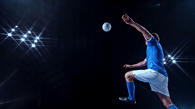 SLO MO LD身穿蓝色球衣的年轻男子足球运动员在黑色背景下用剪刀式踢球视频素材