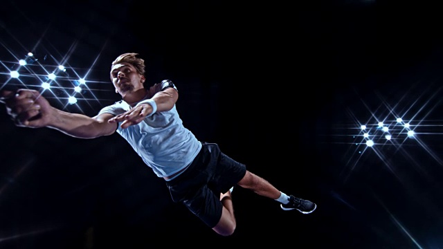 SLO MO男性网球运动员在黑色背景上用球拍跳跃击球视频素材