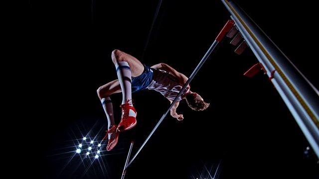 SLO MO男子跳高运动员跳过横杆，落在黑色和红色的垫子上视频素材