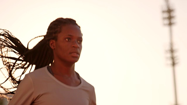 SLO MO DS非裔美国女运动员在日落时在阳光灿烂的体育场跑步视频素材