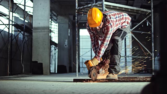 在建筑工地，一名工人正在用角磨机切割地板上的一根金属管视频素材