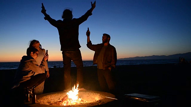 朋友们在海滩篝火上喝啤酒视频素材
