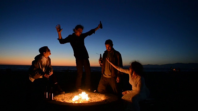 朋友们在海滩篝火上喝啤酒视频素材