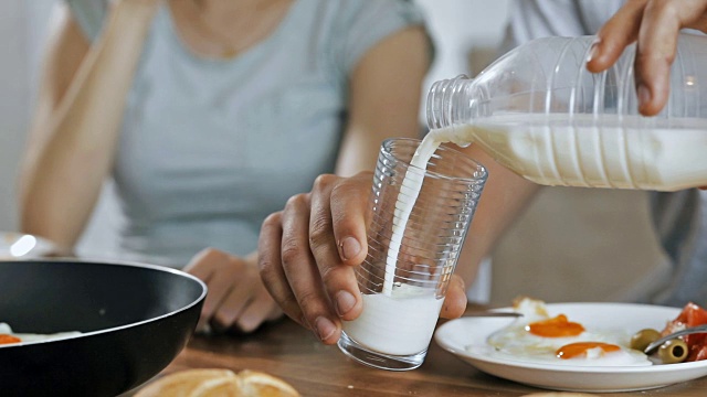 近距离观察一个面目全非的男人在早餐期间把牛奶倒进玻璃杯里。缓慢的运动。视频下载