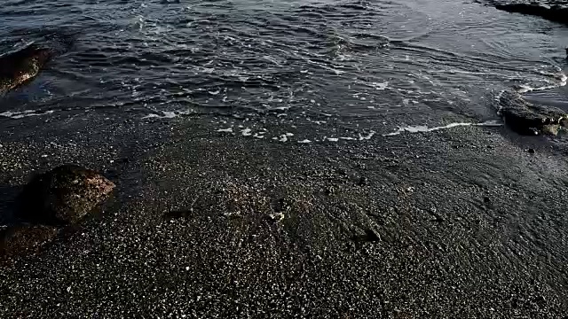 在印尼巴厘岛的黑沙滩上，海浪拍打着沙滩视频素材
