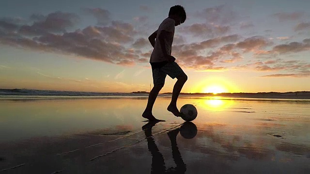 日落时分，男孩在沙滩上踢足球视频素材