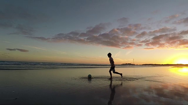 日落时分，男孩在沙滩上踢足球视频素材