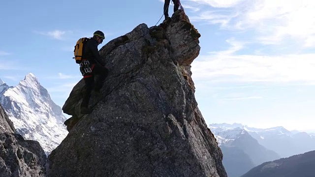 男性登山运动员攀登岩石的顶峰，下面是山脉视频素材