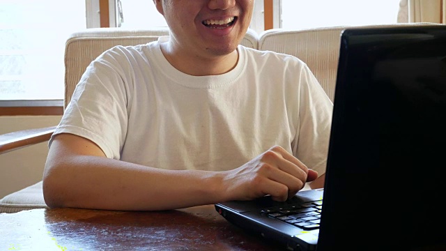 快乐的人在休闲衣服使用笔记本电脑和喝咖啡在客厅-室内场景视频下载