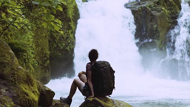 年轻女子在瀑布旁的岩石上休息视频素材