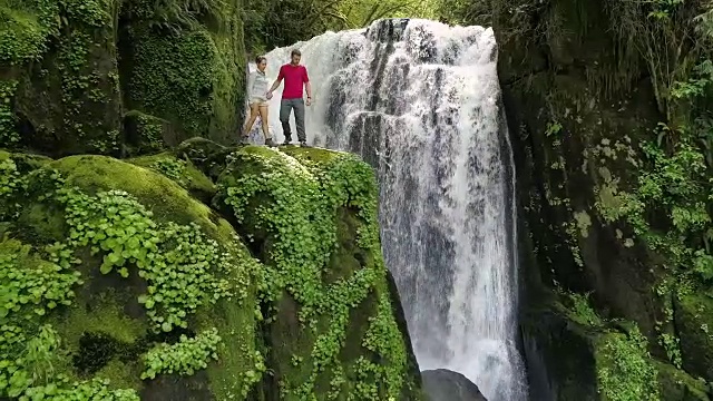 SLO MO夫妇站在悬崖旁边的瀑布视频下载