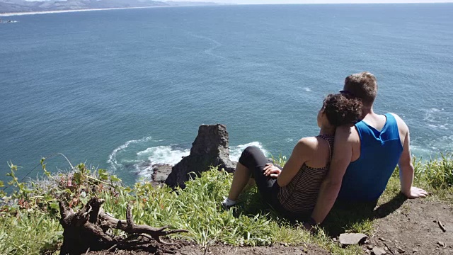 一对年轻夫妇坐在悬崖上俯瞰大海视频下载