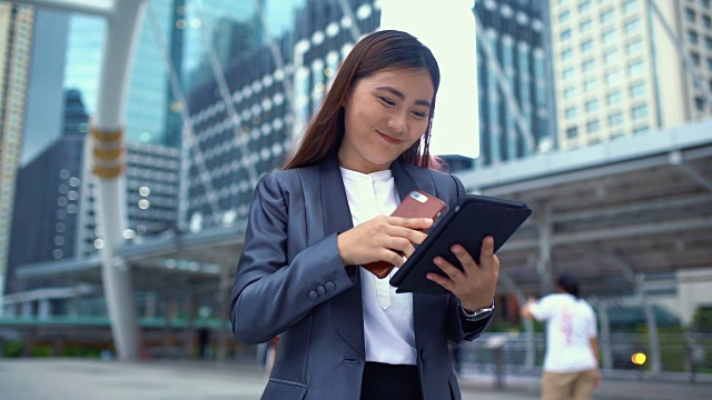 商业女性在城市中使用智能手机和平板电脑视频下载