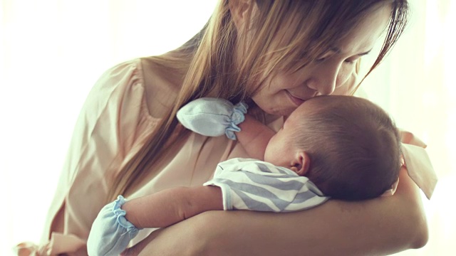 年轻的母亲抱着并亲吻她的新生婴儿视频素材
