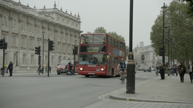 双层巴士在城市街道上靠近唐宁街10号和政府大楼入口的中等角度。白厅SW1。可以看到行人、游客和汽车。妇女二战纪念碑或纪念物可见。视频下载