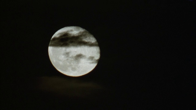 满月在天空中升起的近角度时间流逝。在前景中看到黑色的薄云。月亮从底部开始向上方移动。视频素材