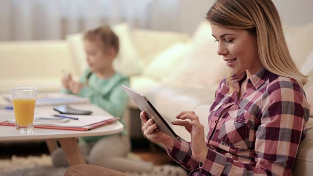 年轻微笑的母亲使用触控板，在家里上网。视频素材