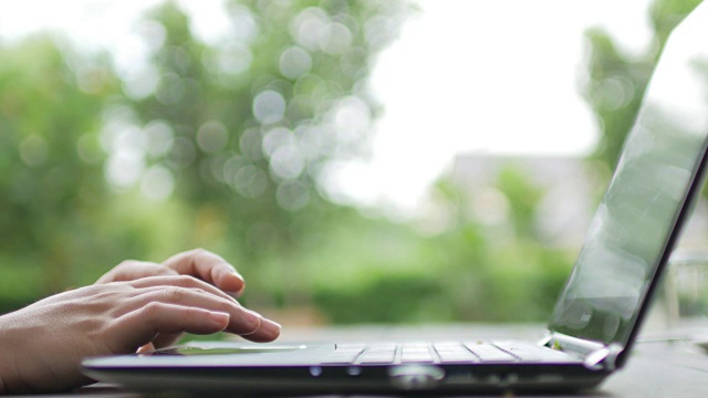 女人用手在户外的笔记本电脑键盘上打字，以绿色的散焦为背景，时光流逝运动视频下载