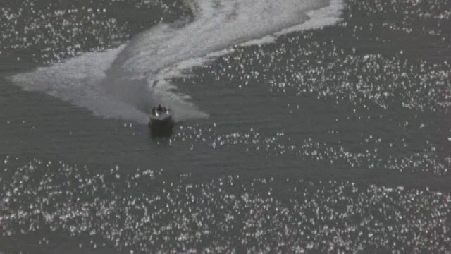 一艘快艇在波光粼粼的水面上急转弯，一架直升飞机在它头顶上追逐它。视频素材