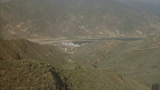 一架直升飞机飞过连绵起伏的山峦，来到一个建筑群。视频下载