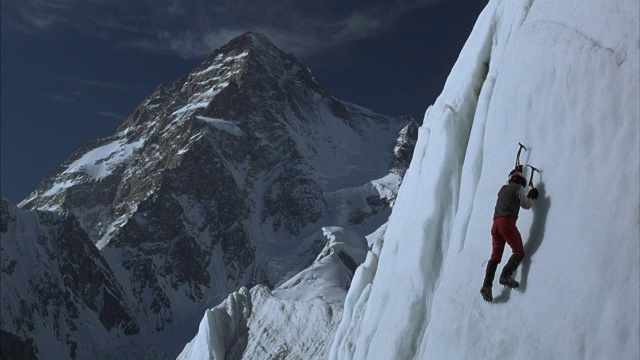 一个冰攀登者用冰斧和冰爪爬上冰墙，背景是一个贫瘠的山脊。视频素材