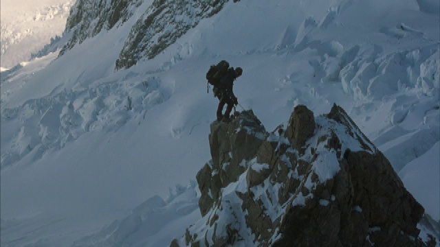 两名登山者爬上白雪覆盖的山脉中间的一个岩石尖顶。视频素材