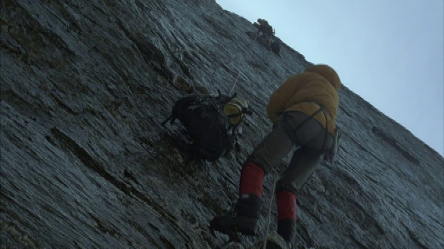 两个登山者攀登岩壁和拖着他们的设备到顶部的特写。视频素材