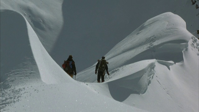 两名登山者在穿越积雪的山脊时缓慢移动。视频素材
