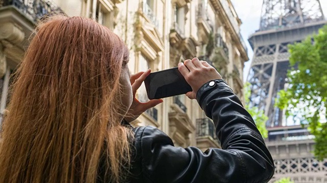 年轻的女游客走在巴黎的街道上，拍下埃菲尔铁塔的照片视频素材