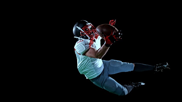 SLO MO穿着白色球衣的美国足球运动员用一只手在黑色背景上接住在空中的球视频下载