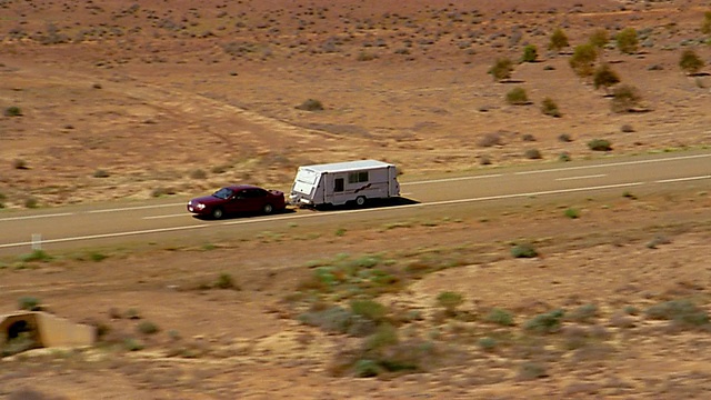 空中跟踪拍摄了沙漠道路上拖着拖车的汽车视频素材