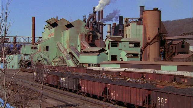 中镜头缩小从烟和烟囱/宽镜头煤炭火车在前景/米尔斯在背景视频素材