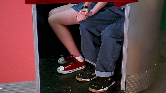 两名青少年的脚和腿在幕布下/手拉手在照相亭视频下载