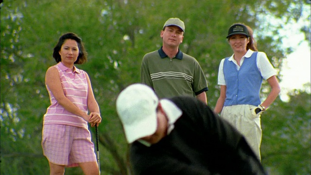 近机架焦点男人打高尔夫球与女人和另一对夫妇看在背景前离开视频素材