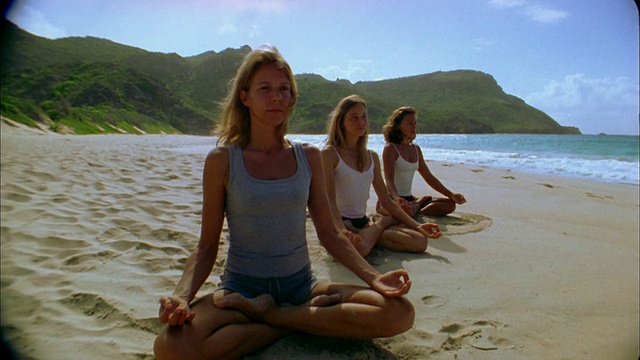 在海滩上做瑜伽时，倾斜下中镜头的女人盘腿而坐视频下载