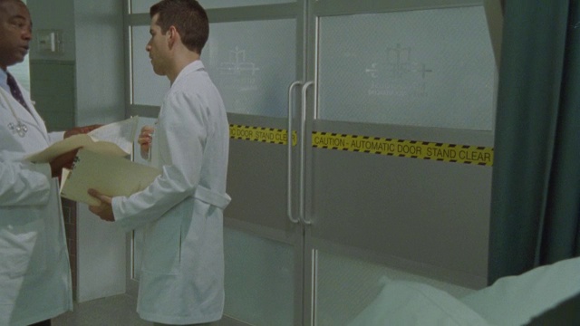 两名医生在急诊室门口交谈并查看记录。视频素材