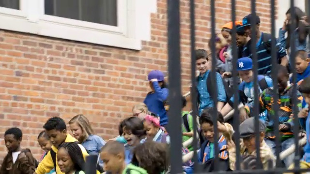 中等角度的孩子或孩子离开学校。孩子们跑下楼梯来到人行道上。警察或警卫可见。视频下载