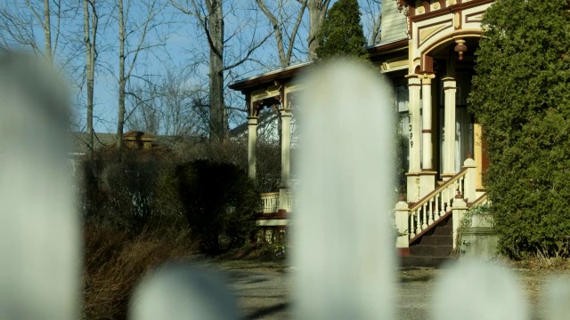 中等角度的多层维多利亚房屋通过栅栏柱。可见乔木和灌木。视频下载