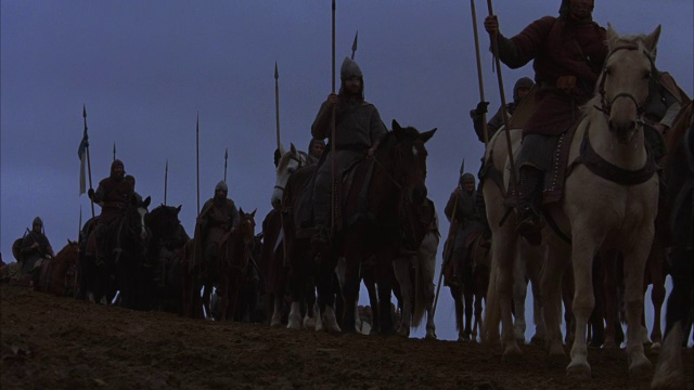 骑士在土丘上旅行的广角。骑士骑在马背上，其他人在bg中行进。骑士身穿盔甲，手持旗帜、盾牌和长矛。在游行队伍的末尾可以看到一个大十字架。可以让骑士去打仗。视频素材