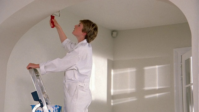 中镜头女人在梯子上刷墙/停下来，用正手擦，爬下来，留下油漆桶视频下载