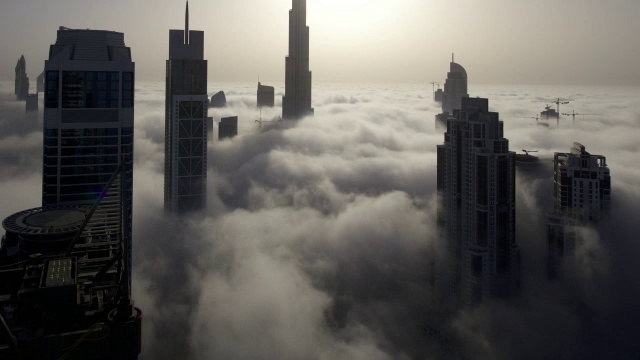 当太阳在迪拜的哈利法塔(Burj Khalifa)后面升起时，一层一层的雾在摩天大楼之间飘过视频素材