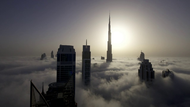 当太阳在迪拜的哈利法塔(Burj Khalifa)后面升起时，一层一层的雾在摩天大楼之间飘过视频素材
