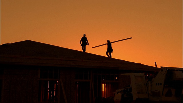 两个建筑工人在屋顶上搬运木板的中景剪影/凤凰城，亚利桑那州视频下载