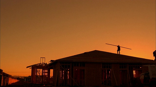 两个建筑工人在屋顶上搬运木板的剪影/凤凰城，亚利桑那州视频素材