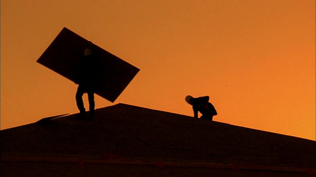 建筑工人在屋顶上搬运木板的中景剪影/亚利桑那州凤凰城视频素材