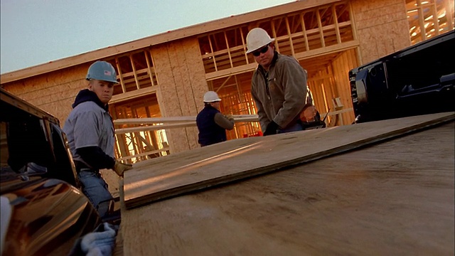 在亚利桑那州凤凰城，两名建筑工人正在从卡车上卸载木板视频素材