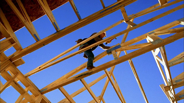 低角度中拍摄建筑工人锤击房屋框架/蓝天背景/凤凰城，亚利桑那州视频素材