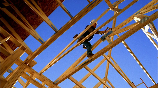 低角度中拍摄建筑工人锤击房屋框架/蓝天背景/凤凰城，亚利桑那州视频素材